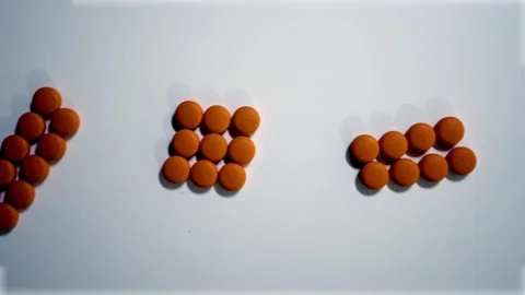 Orange pills in decreasing groups on white background overhead panning shot Stock-Footage 337244182