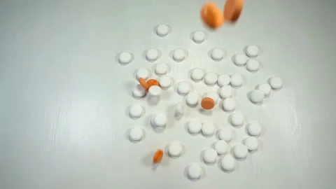 Orange pills fall on a pile of white pills in slow motion. Stock Footage 164215372