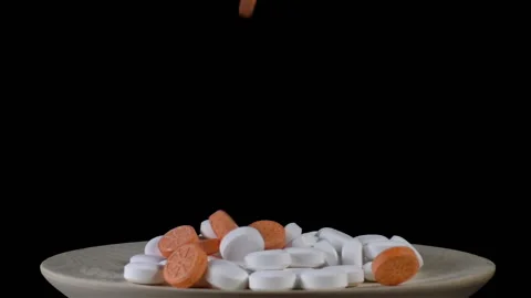 Orange pills falling in slow motion on plate Stock Footage 141498204