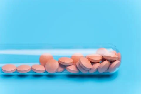 Orange pills or tablets drop out of the test tube on blue background Stock Photos