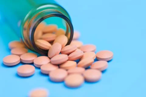 Orange pills or tablets drop out of the brown glass bottle on blue background Stock Photos