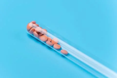 Orange pills or tablets drop out of the test tube on blue background Stock Photos