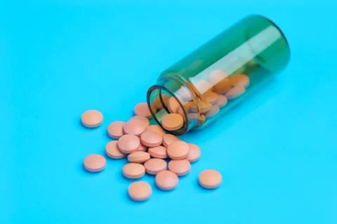 Orange pills or tablets drop out of the brown glass bottle on blue background Stock Photos