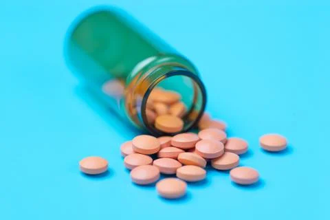 Orange pills or tablets drop out of the brown glass bottle on blue background Stock Photos