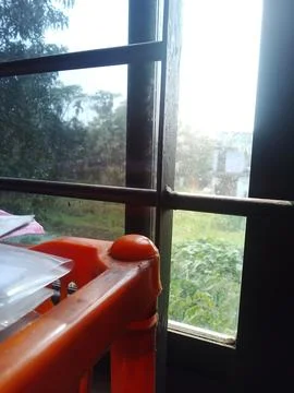 Orange plastic bookshelf positioned by window frame with green garden view Stock Photos