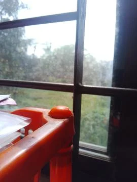 Orange plastic bookshelf positioned by window frame with green garden view Stock Photos