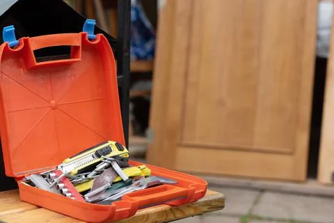 Orange plastic box with toolkit on bench against wooden door Stock Photos