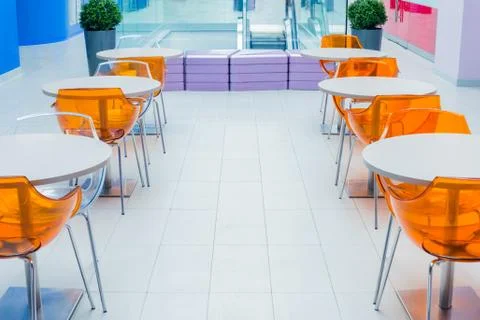 Orange plastic chairs and a white table on food court Stock Photos