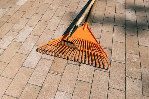 Orange plastic lawn leaf rake lying on stone paved walkway outdoors Photos