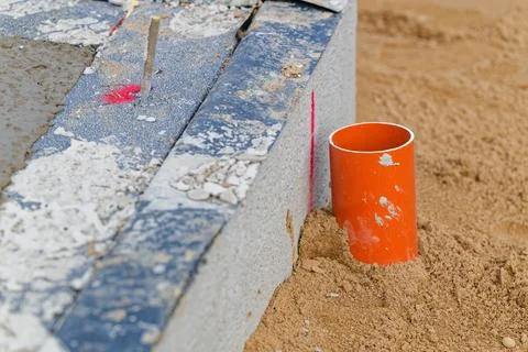 Orange plastic pipe embedded in sandy ground beside concrete foundation wit.. Stock Photos