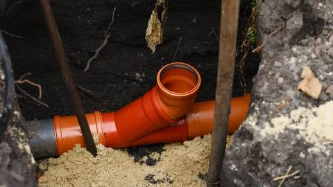An orange plastic sewer pipe fitting installed in a deep dirt trench Stock Photos