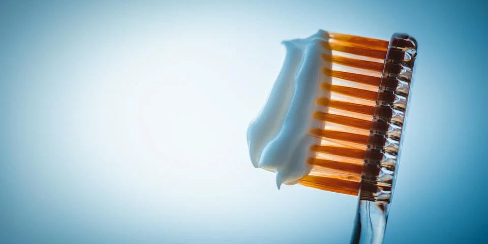 Orange plastic toothbrush with a thick layer of white toothpaste on a blue ba Photos