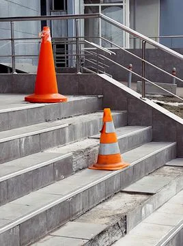 Orange protective cones on broken steps in office building warn of danger. Stock Photos