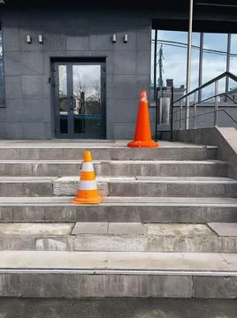 Orange protective cones on broken steps at entrance to office building warn of Stock Photos