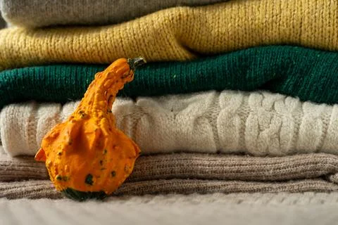 Orange pumpkin near a stack of knitted sweaters on a knitted blanket Foto stock