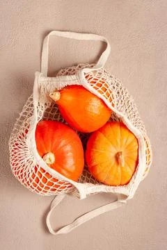 Orange pumpkins in a string bag on a beige background 스톡 사진