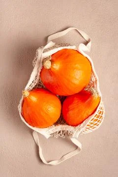 Orange pumpkins in a string bag on a beige background Stock Photos