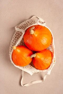Orange pumpkins in a string bag on a beige background Stock Photos