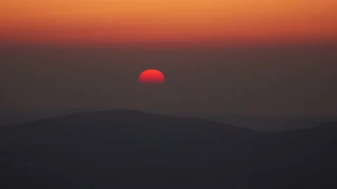 An orange red half sun dipping into the mountain landscape of Snowdonia 動画素材 173403934