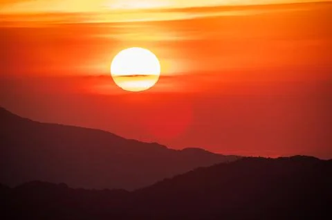 The orange-red sunset is covered by clouds as it moves towards the horizon. Stock Photos