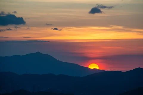 The orange-red sunset is covered by clouds as it moves towards the horizon. Stock Photos