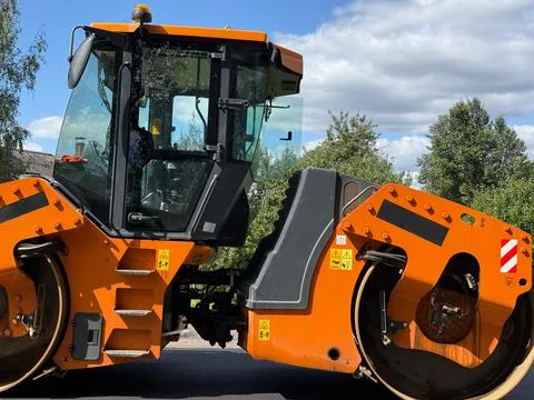 Orange road roller compacting asphalt on a new road concept of construction a Stock Photos
