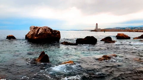 Orange rocks at bay with lighthouse in the background Stock Footage 90551366