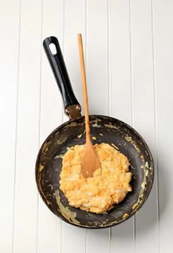 Orange scrambled eggs in a black pan with spatula Stock Photos