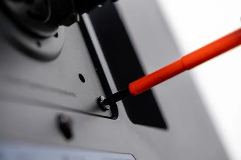 Orange screwdriver turns a silver screw on dark device panel, symbolizing d.. Stock Photos