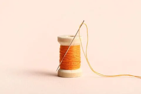 Orange sewing thread with needle on beige background Stock Photos