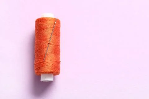Orange sewing thread with needle on lilac background Stock Photos