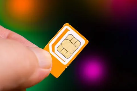 Orange sim card held between fingers with colorful bokeh background Stock Photos