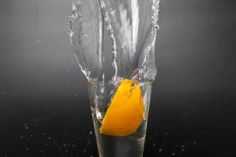 Orange slice falling and dropping into a splashing glass with black backgroun Stock Photos