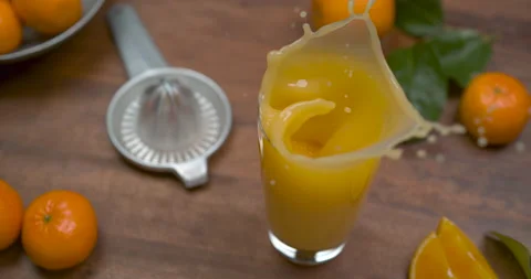 Orange slice falling in a tall glass of orange juice, on a wooden table decorate Video stock 199461609