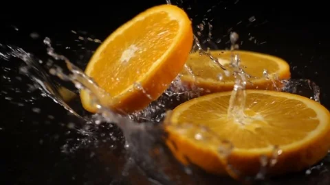 Orange slices fall on the black surface covered with water Stock Footage 71107837