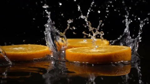 Orange slices fall on the black surface covered with water Stock Footage 71108822