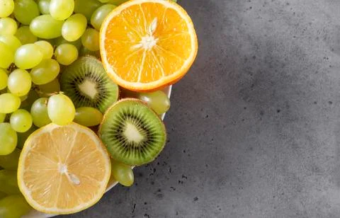 Orange slices, green grapes, kiwi, lemon slices on a gray background, fresh c Stock Photos