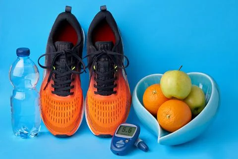 Orange sneakers, glucometer, bottle of drinking water and fruits on blue back Stock Photos