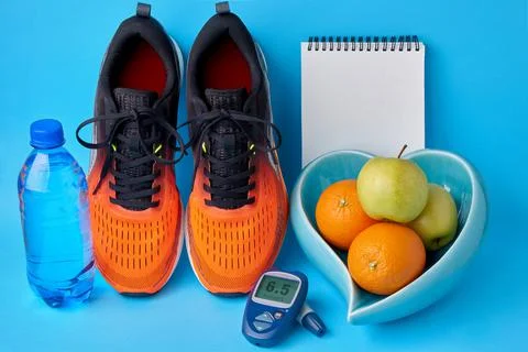 Orange sneakers, a notebook, a glucometer, a bottle of drinking water and fru Stock Photos