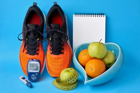 Orange sneakers, notepad, glucometer, measuring tape and fruit in a heart-shaped Foto stock