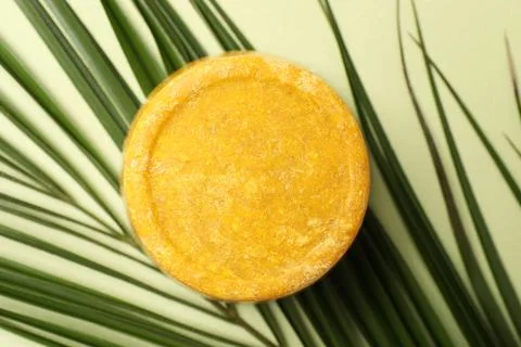 Orange solid shampoo bar and leaf on green background, top view. Hair care Stock Photos