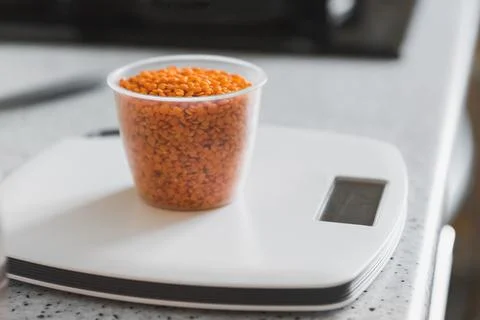 Orange split lentils in a plastic measuring cup on white digital kitchen scale Stock Photos