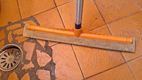 Orange sponge floor squeegee cleaning wet brown tiled bathroom floor Stock Photos