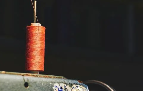 Orange spool of thread on an old gray sewing machine and a dark background Stock Photos