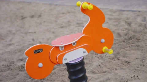 Orange spring rider stands ready on sandy playground Stock Footage 332116223