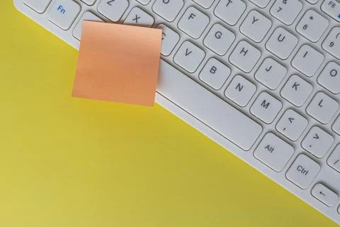 Orange sticky note on top of white keyboard. Flat lay. Copy space. Stock Photos
