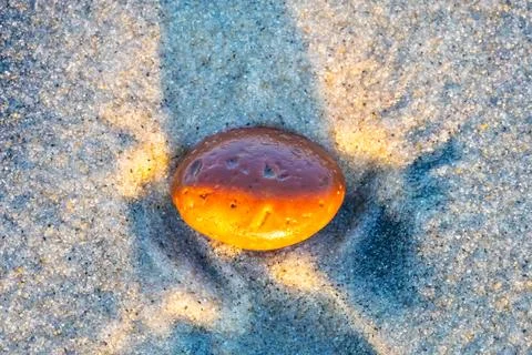 Orange stone on the sand with long shadow, closeup Stock Photos
