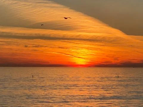 Orange sun behind clouds over Ocean Stock Photos