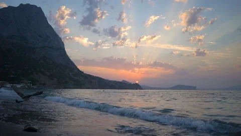 Orange sun disk sets behind rocky coastal hill above sea Video stock 102664482