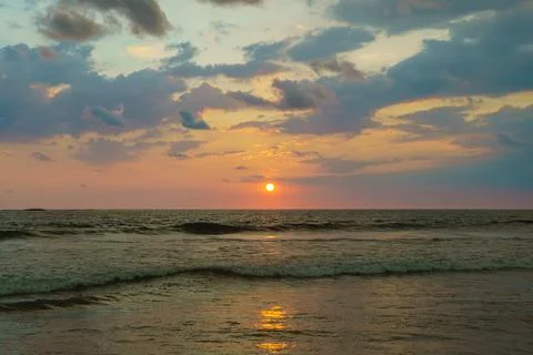 The orange sun sets against the backdrop of the sea and clouds Stock Photos